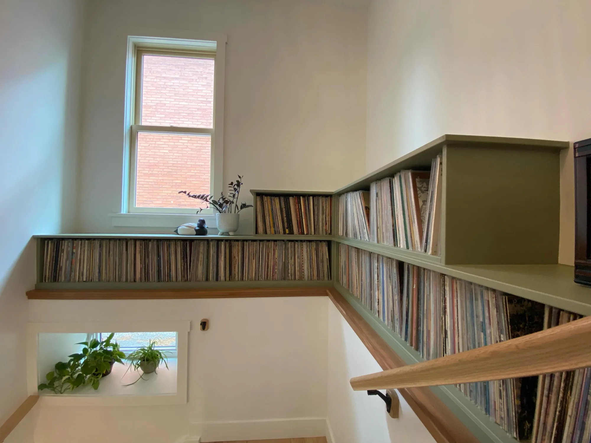 Custom green record shelving built into a stairwell beneath a window